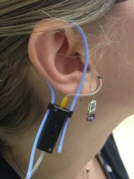 A real ear microphone inserted into a person's ear canal, featuring a thin wire and a small black device.
