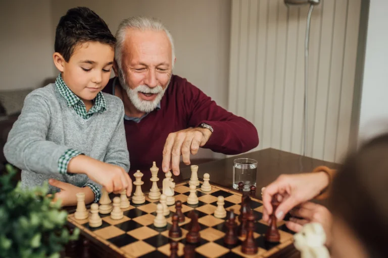 A senior man plays chess with his grandson