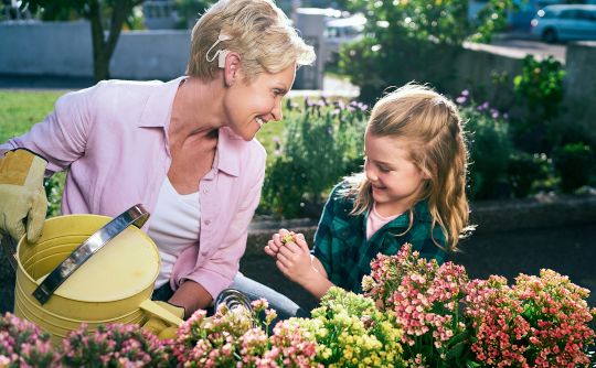A mature woman with cochlear implants gardening with her granddaughter