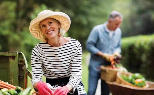 A mature woman gardening with her husband in the background
